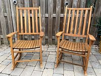 Front view of both chairs side by side on stone pavers against wooden fence