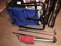 Photo showing folded AB Lounger with blue fabric and black metal frame, five golf clubs on the floor, and red golf ball collector bag.