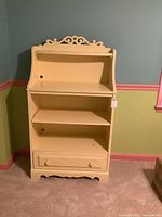 Front view of cream painted 3-shelf Stanley bookcase with a drawer at the bottom and decorative cutouts on the side panels.