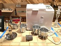 Oster bread machine with accessories on tiled surface. Label with '466' and 'bread machine cutter grater' on bread machine.