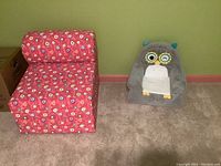 Both chairs side by side on carpeted floor against green wall with pink baseboard: pink floral foam chair on left, gray owl chair on right