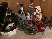 Multiple Christmas wreaths, artificial greenery, metal snowman sign, wreath decorations and red ribbon bows on the floor
