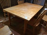 Overview of the heavy wood rectangular dining table surrounded by six matching chairs showing the light natural wood finish and turned legs.