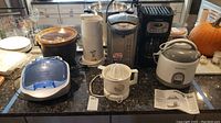 Full overview of kitchen appliances on a granite countertop, including rice cooker, slow cooker, water boiler, juicer, coffee maker and more.