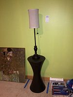 Front view of lamp standing on hourglass-shaped metal table with beige fabric lampshade and pull chain switch