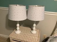 Pair of white ceramic base lamps with white rhinestone-studded shades on a wicker table underneath wainscoting and teal wall.
