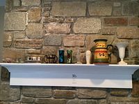 Wide view of mantel displaying all items in lot: Lenox urn style vase, bud vase, Ceskci crystal candlestick, metal pillar candle holder, coloured votive holders.