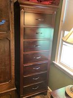 Full view of the tall lingerie chest showing seven drawers with metal handles and carved top molding.