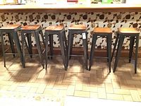 Six metal stools in a row beneath a countertop, four taller on left and two shorter on right.