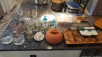 Overview of lot showing glassware, mixing bowls, serving trays, plastic molds, ceramic container, and other kitchen items laid out on countertop.