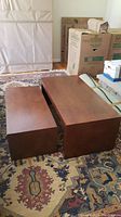 Two rectangular wood nesting coffee tables placed side-by-side on patterned rug near packing boxes and furniture.