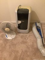 AeonAir portable air conditioner on carpet next to a white Living Accents table fan and an exhausted hose laid out on the floor.