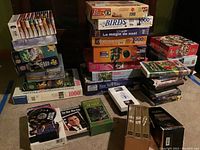 Puzzles, VHS and DVD tapes stacked on floor, showing quantity and variety.