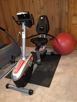Overview of recumbent stationary exercise bike on floor mat with red exercise ball in background
