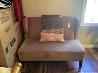 Front view of upholstered settee with patchwork throw pillows on seat. Shows color, material, nailhead trim, and wood legs.