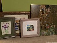 Four framed artworks set against a green wall, including the seriolithograph-by Picot, the Kiss poster, and two watercolors.