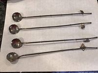 Four long handle sterling spoons laid side by side showing scalloped bowls and charms attached near the end of each handle.