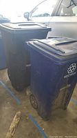 Photo showing blue recycling bin and black trash can side by side