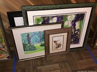 Four framed watercolor prints positioned leaning against a wall showing the variety in size, frame styles, and artistic themes.