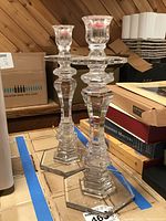Two clear Waterford crystal candlestick holders standing on a table surrounded by boxes. Bases show some scratches on their bottoms.