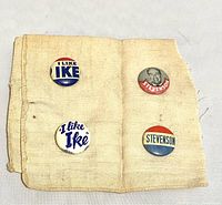 Four political campaign buttons pinned to a used off-white handkerchief, two for Eisenhower with 'I LIKE IKE' slogans and two for Stevenson including a portrait button.