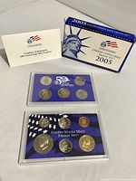 Overall view of 2005 US Mint proof set box, certificate of authenticity, and two plastic cases with proof coins including five state quarters and base set coins.