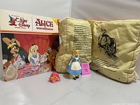 Photo showing the Alice ceramic figure in blue dress, Cheshire Cat ceramic figure, Alice in Wonderland laserdisc cover, and Alice in Wonderland pillow