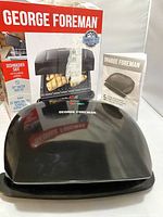 Closed black George Foreman grill with original box and instruction manual behind it