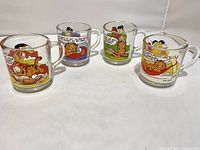 All four Garfield glass mugs arranged side by side showing different Garfield comic art and colors.
