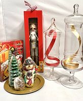 Photo showing the holiday mantle decor set including large and medium glass canisters with ribbons, handmade nutcracker in box, and holiday candle set with gold tray