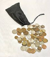 Full view of black drawstring fabric sack with approximately 40 mixed metal international coins spilled in front of it, showing varying sizes and colors.