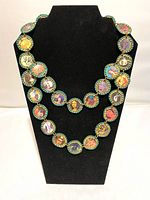 Full view of Recology necklace displayed on black bust, showing flattened bottle caps with colorful artwork inside.