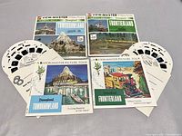 Photo showing two View-Master packets for Disneyland's Tomorrowland and Frontierland each with three reels, envelope, and booklet spread out.