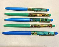 Five vintage floaty bubble pens laid flat with visible colorful liquid-filled bubble segments depicting various travel scenes and locations, including Holland, Palm Desert, Gatorland Orlando, I Love New York, and Roaring Camp Railroad
