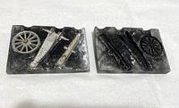 Photo of the two halves of the vintage lead cannon mold showing cavities for cannon barrels and wheels with dark, worn surfaces.