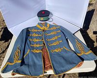 Front view of the light blue vintage military costume jacket with gold braided detailing and matching cap on a table outdoors.