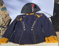 Front view of the dark blue military costume jacket laid flat with black hat with red and black plume placed behind the collar area.