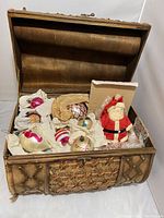 Vintage chest open showing glass Christmas ornaments, Santa figurine, and small animal ornament inside.