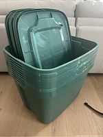 Stack of 11 green storage bin lids shown sitting on top of the bins on a wooden floor.
