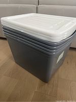 Stack of four large grey storage bins with white lids, showing size and condition.