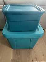 Four turquoise plastic storage bins stacked, showing three large bins with lids and one medium bin with lid on top of a large bin.