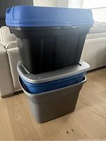 Photo showing a stack of large storage bins, three bins with lids and one lidless bin visible.