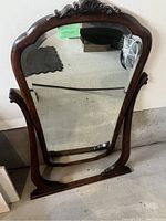 Full view of the antique mirror showing wooden frame, ornate carved crest on top, and easel back stand.