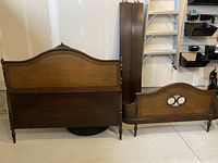 Photo of disassembled solid wood Art Deco double bed frame showing headboard and footboard leaning against wall.