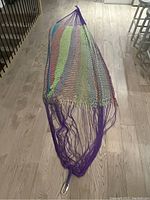 Full view of the woven hammock showing its overall shape and purple ends with metal hooks.