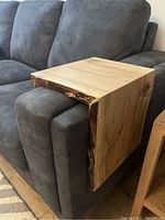 Sofa cuff link placed over grey fabric sofa armrest showing live edge ambrosia maple wood with natural grain and edge details.