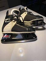 Pair of men's ice hockey skates with black and white design, size 8.5, shown from side angle on a tabletop.