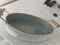 Gray metal tray with white diamond and floral pattern on sides, wood handles visible. Tray shown on white stone countertop.