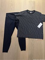Photo of the full lot showing the striped black and white All Yours tee and black leggings with wave pattern laid on floor.