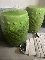 Pair of green ceramic stools with textured designs and glossy finish shown on floor with protective wrapping nearby